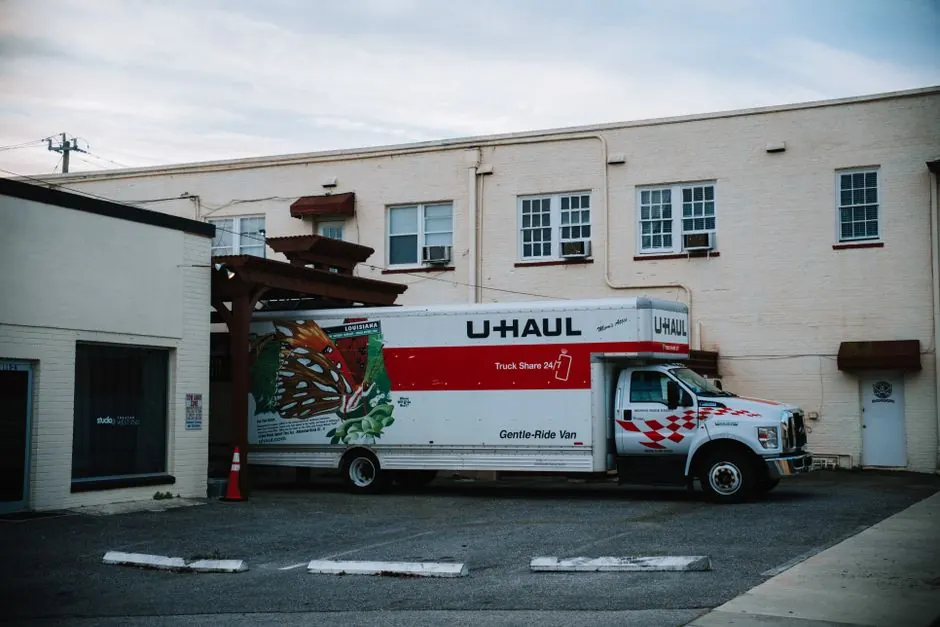 A U-Haul moving truck parked in front of a beige warehouse building.